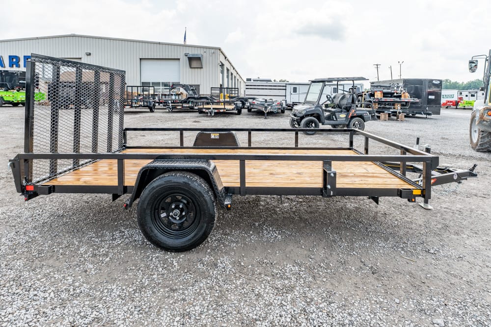 Flatbed utility trailer with wooden deck and mesh rear gate on a gravel lot.
