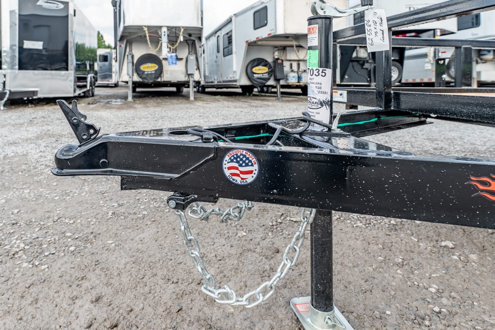 Close-up of a black trailer hitch with a silver safety chain, in a gravel lot with RVs in the background, a 'Proudly Made in USA' sticker visible on the hitch.