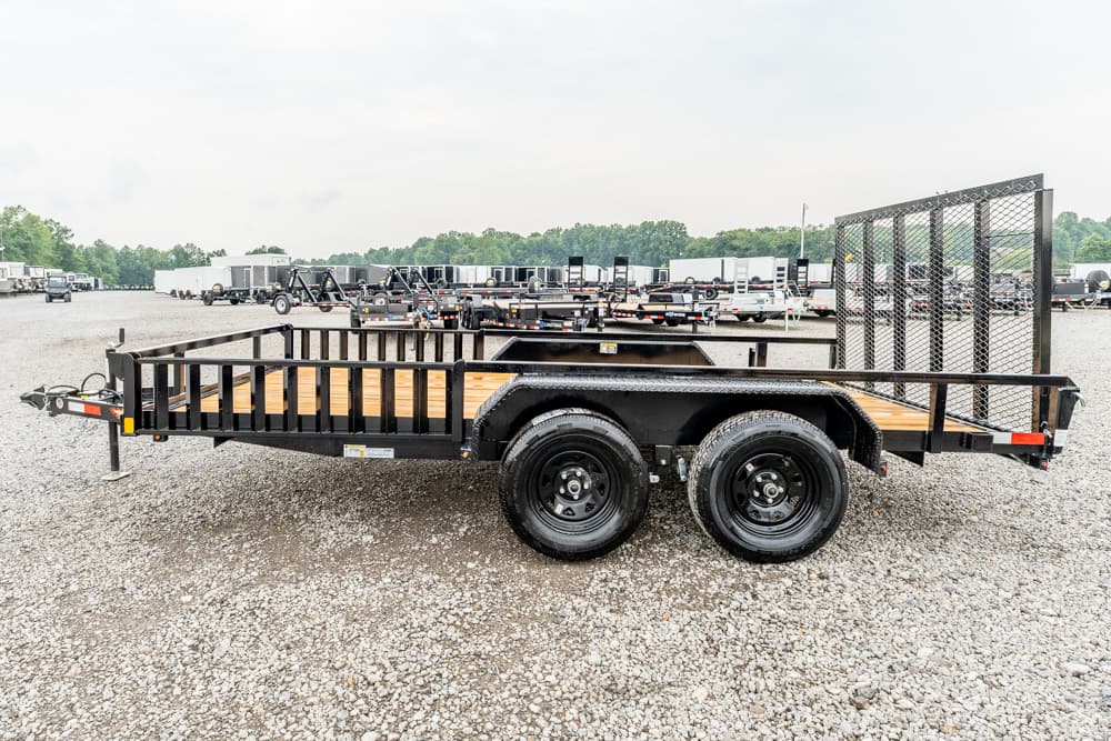 Black dual-axle utility trailer with wooden deck and side rails in a gravel lot footprint
