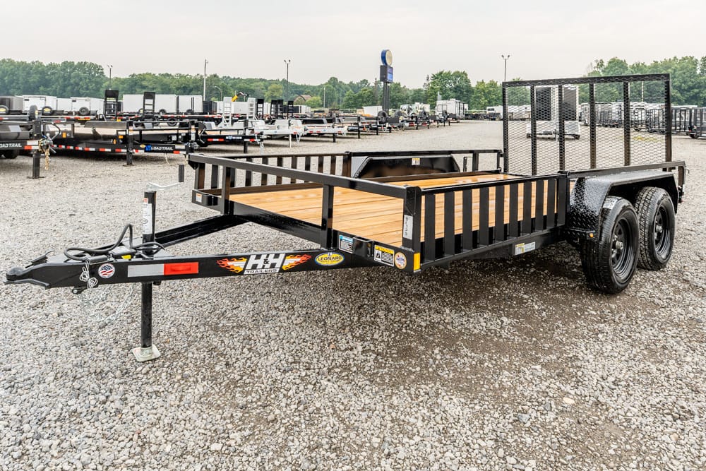 Black utility trailer with wooden deck and tall side rails on a gravel lot, dual-axle with a ramp gate at the rear