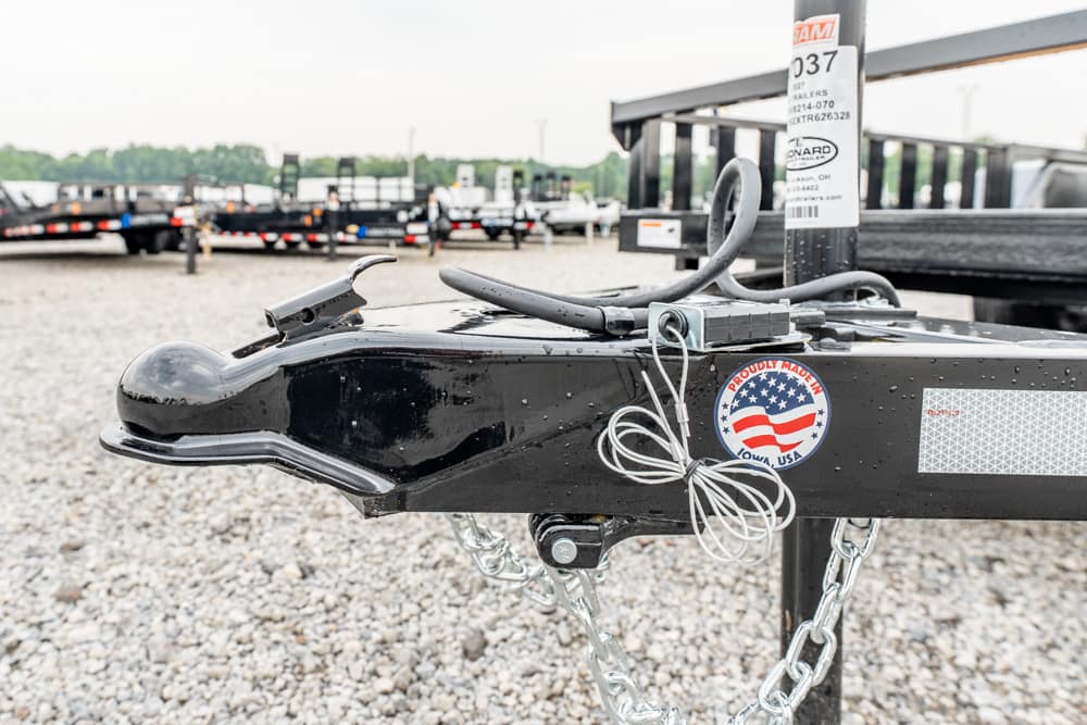 Close-up of a black trailer hitch with safety chains on a gravel lot.