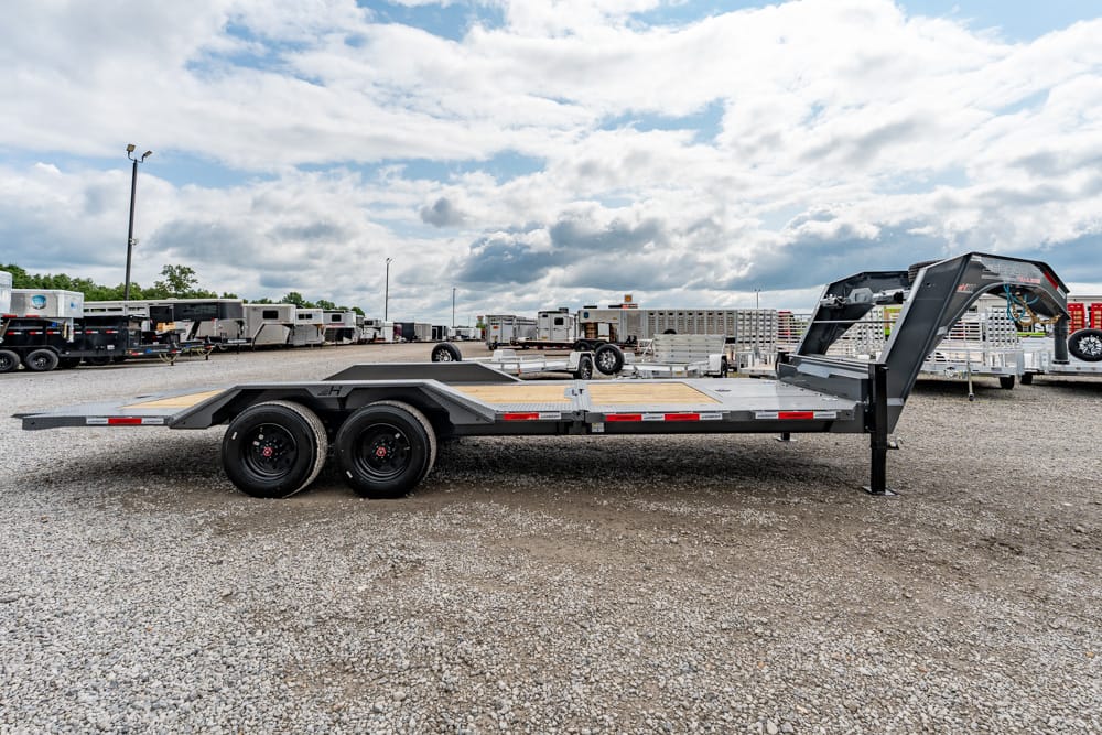 Long flatbed trailer with dual axles and a gooseneck hitch parked in a gravel trailer lot