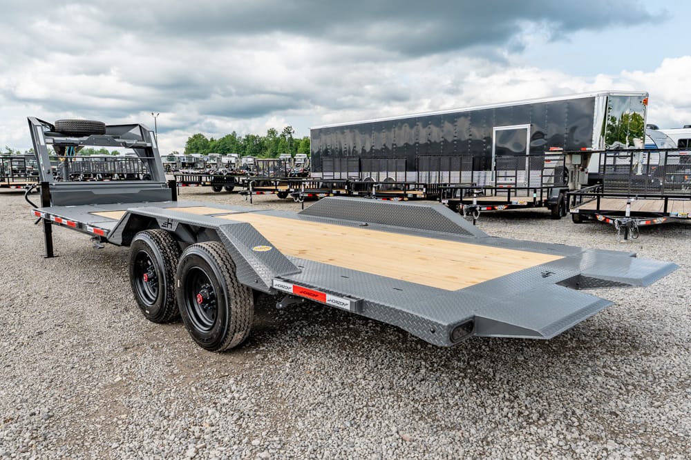Flatbed trailer with a wood deck and dual rear axles parked in a trailer lot.