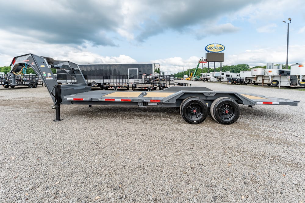 Dual-axle flatbed trailer with a front-mounted ramp on a gravel lot, surrounded by other trailers and trucks in a yard.