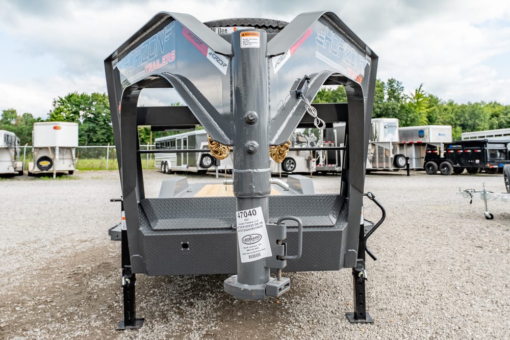 Front view of a gray gooseneck trailer hitch and platform on gravel, with other trailers in the background.