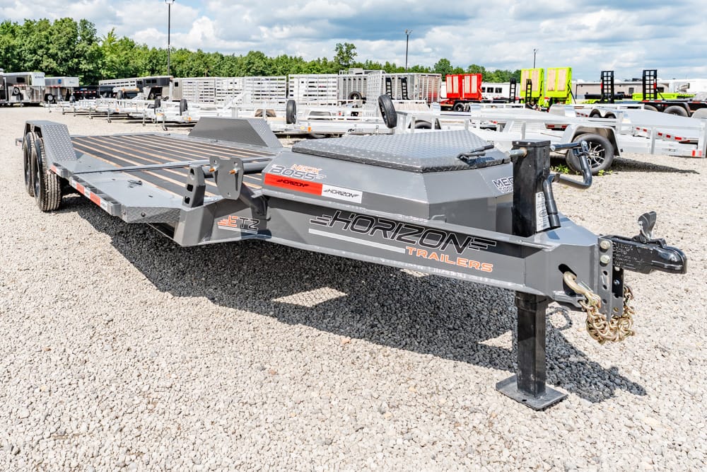 Grey Horizon Trailers flatbed trailer with dual axles on a gravel lot, hitch and safety chains visible at the front.