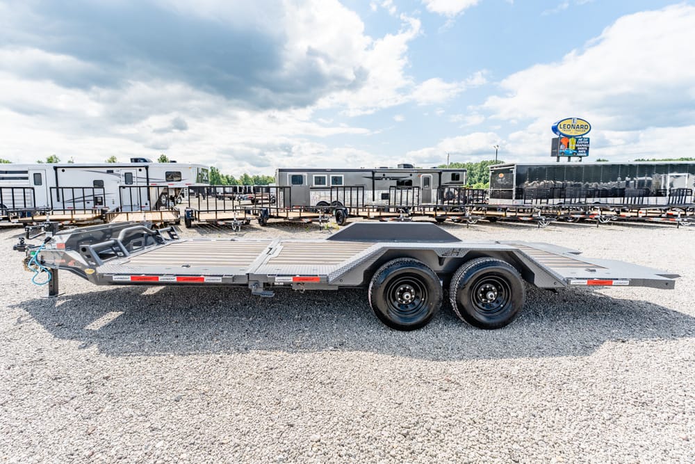 Flatbed car trailer with dual axles on a gravel lot, surrounded by other trailers under a cloudy sky.
