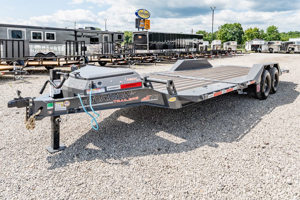 Long flatbed car trailer with dual axles on a gravel lot, Horizon Trailers branding, with other trailers in the background.