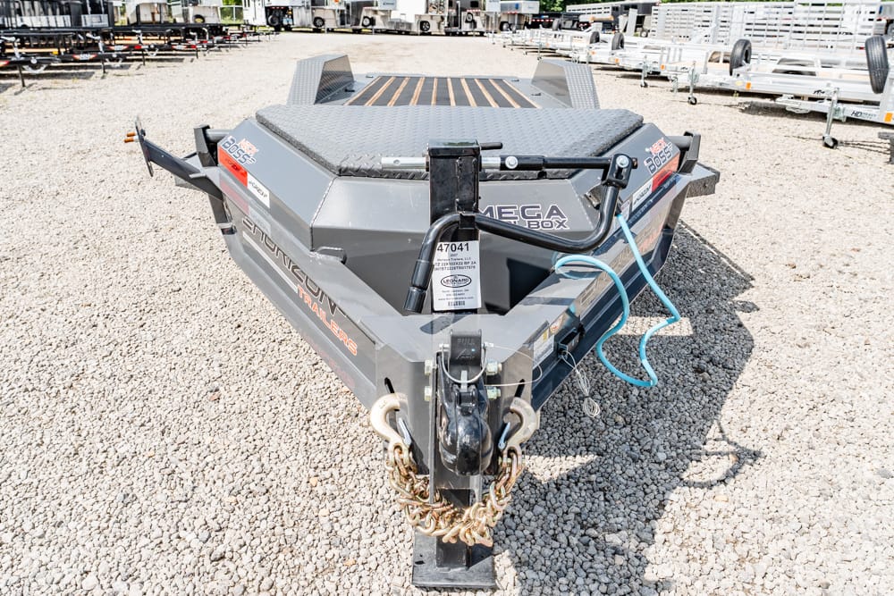 Front view of a gray Mega Box equipment trailer on a gravel lot, hitch and safety chains visible, with a blue hose coiled on the side.