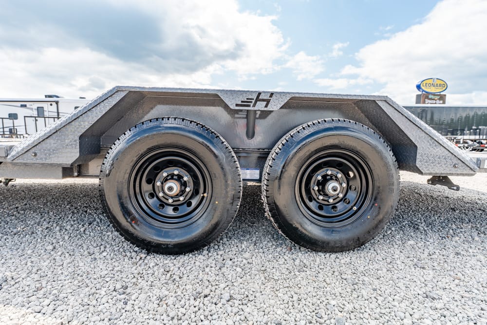 Dual-axle utility trailer with diamond-plate fenders on a gravel lot under a blue sky