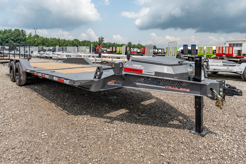 Grey Horizon Trailers flatbed trailer with dual axles on a gravel lot, other trailers visible in the background, branding on the side.