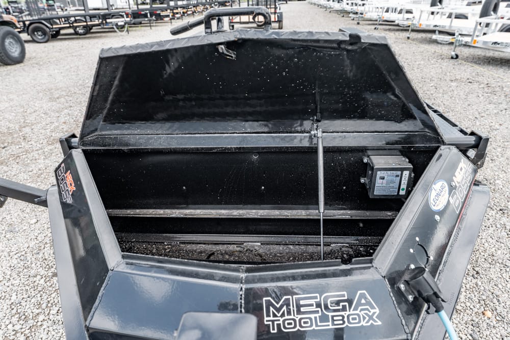 Open Mega Toolbox trailer bed with an empty black interior and a control panel on the right, parked on a gravel lot beneath other trailers.
