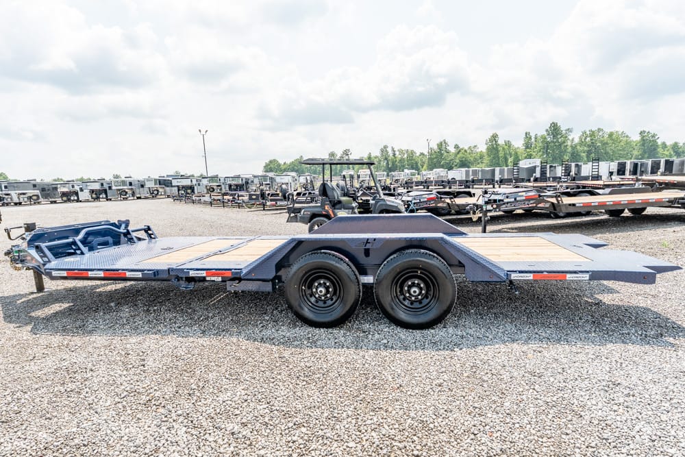 Blue-gray flatbed car trailer with dual rear axles in a gravel trailer yard