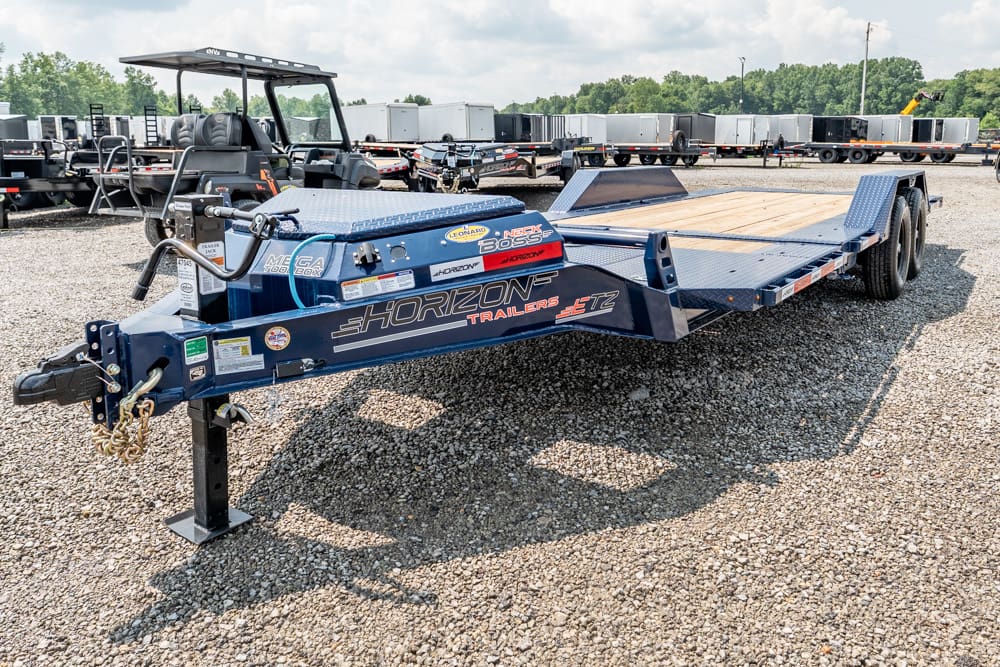 Blue Horizon Trailers equipment trailer with wooden decking parked on gravel yard; front hitch and dual tandem axles visible.