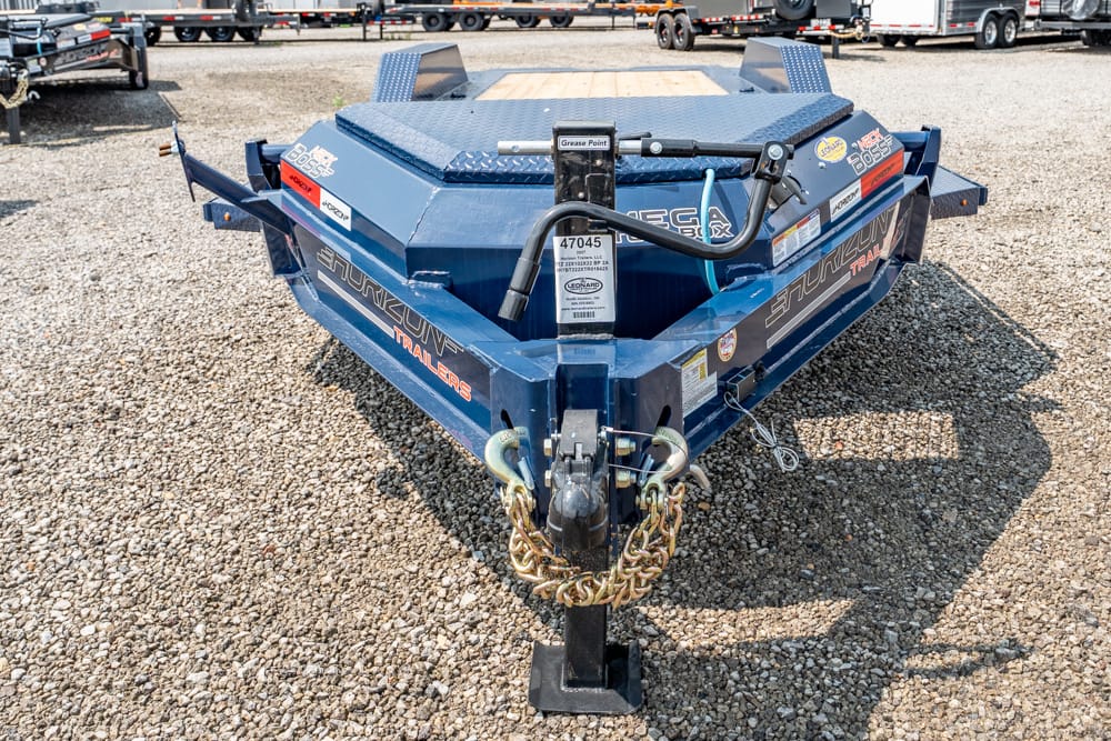 Front view of a blue heavy-duty trailer hitch on a gravel lot, with safety chains and a coupler ready to tow.