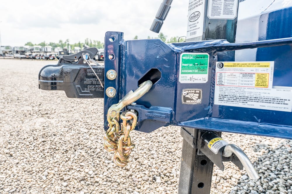 Close-up of a blue trailer hitch with a heavy chain and padlock on a gravel lot, ready for towing.