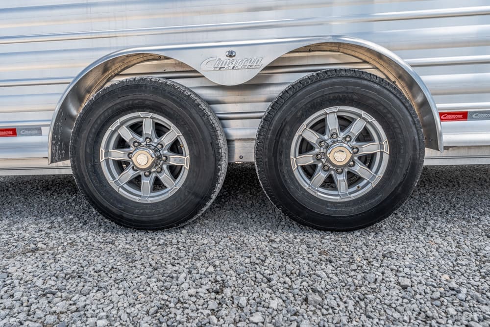 Double-axle trailer with metal fenders and silver wheels on a gravel lot