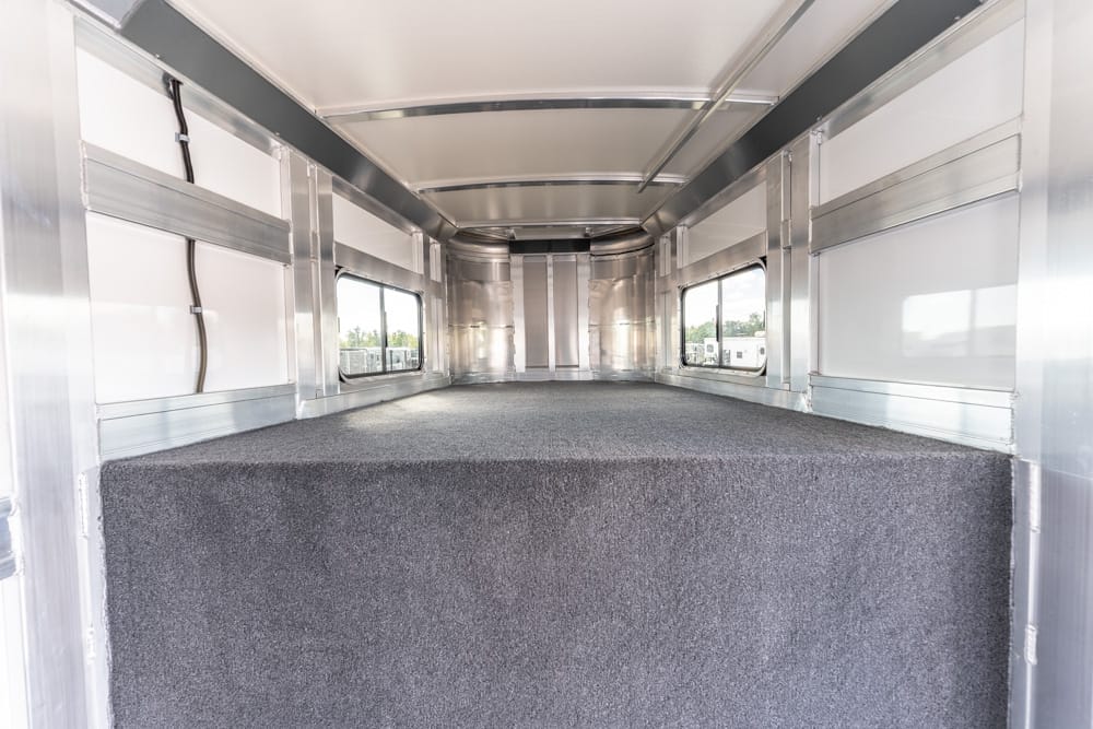 Interior of an aluminum trailer with a gray carpeted loading platform, side windows, and metal framing along both walls.