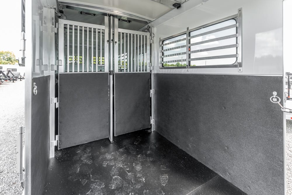 Interior of a horse trailer with two partitioned stalls and rubber flooring, awaiting horses