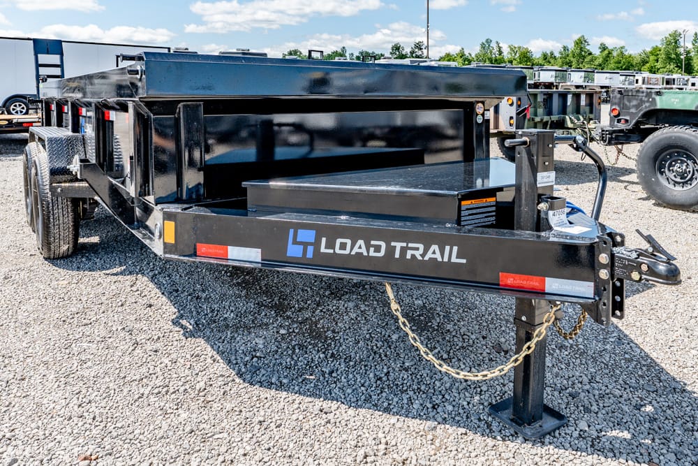 Black Load Trail equipment trailer on gravel with open bed and loading ramp, dual axles, and chain secured hitch area, brand visible.