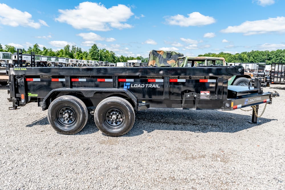 Black Load Trail dual-axle dump trailer on a gravel lot with other trailers in the background.