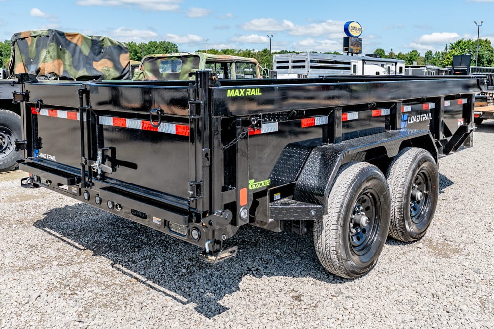 Black Load Trail Max Rail dump trailer with tandem axles and diamond-plate fenders on a gravel lot, camo-covered toolbox.