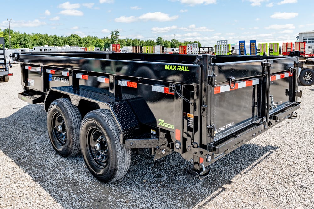 Black tandem-axle dump trailer with reflective stripes parked on a gravel lot, side rails and rear gate visible