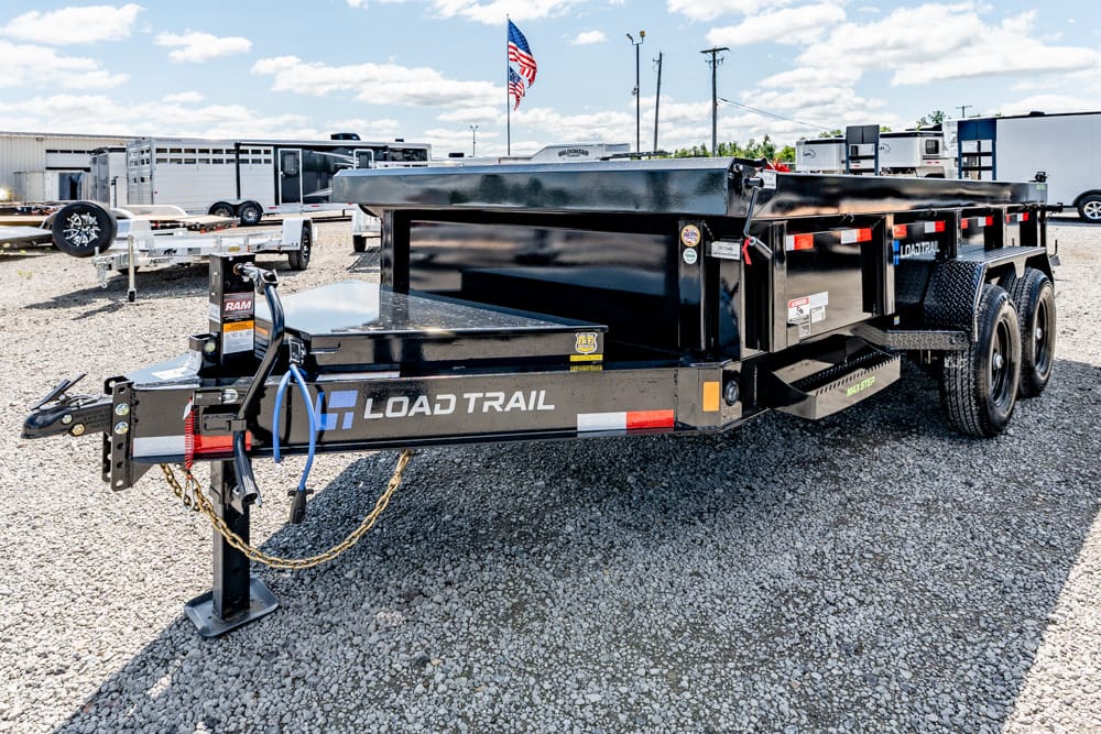 Black Load Trail dual-axle trailer on a gravel lot, with a raised flatbed and safety chains visible at the hitch.