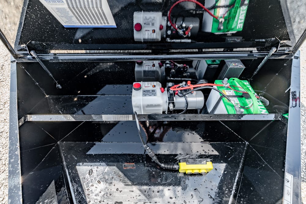 Industrial generator inside a black metal compartment with a battery, red/black wires, and a yellow power connector visible on the wet floor of the box.