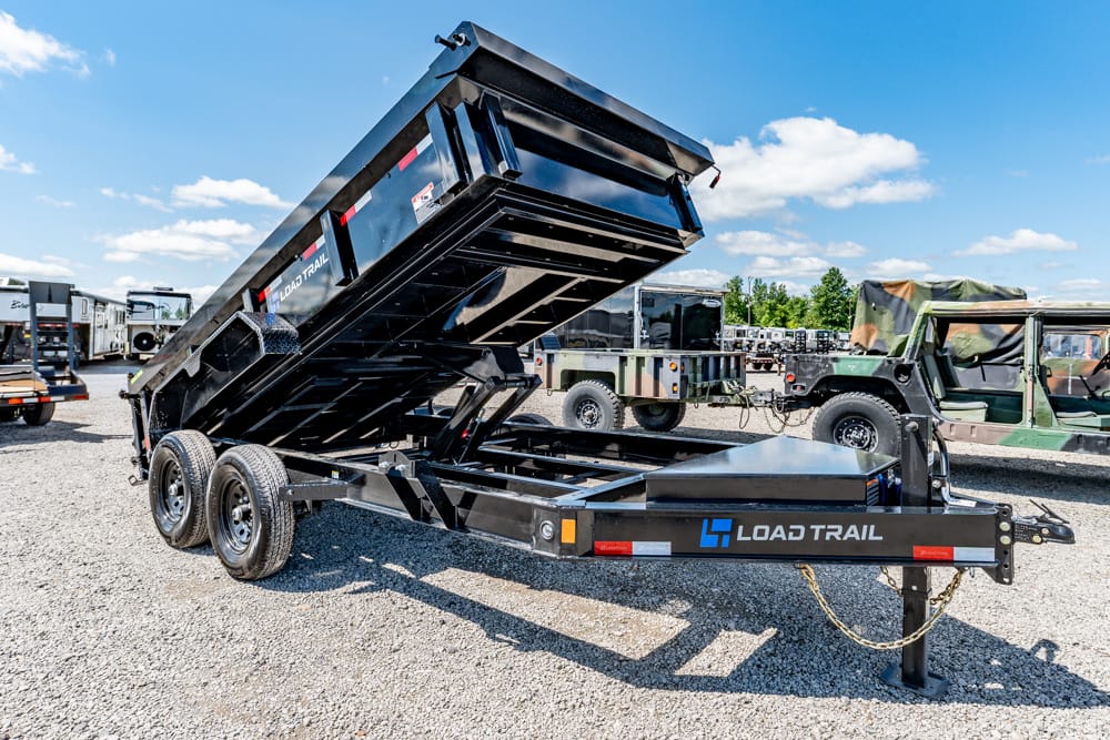 Black Load Trail hydraulic dump trailer with raised bed on a gravel lot, dual-axle, outdoors.