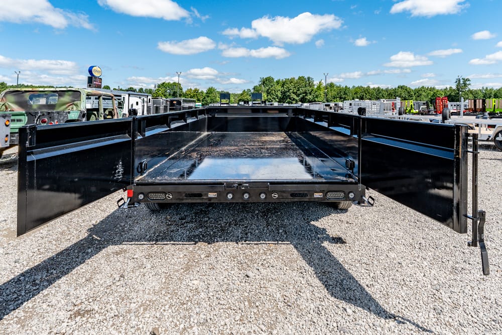 Black dump trailer with side and rear gates fully open in a gravel lot, ready to load materials.