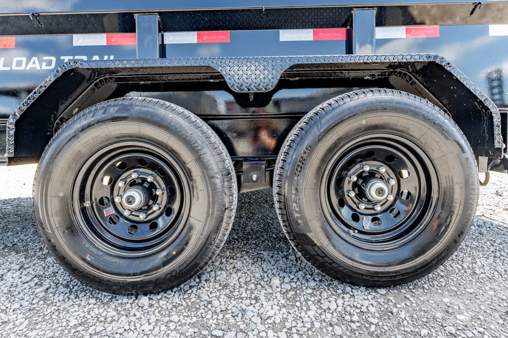Dual trailer wheels with black steel rims on a gravel surface, close-up view of tires and hubs.