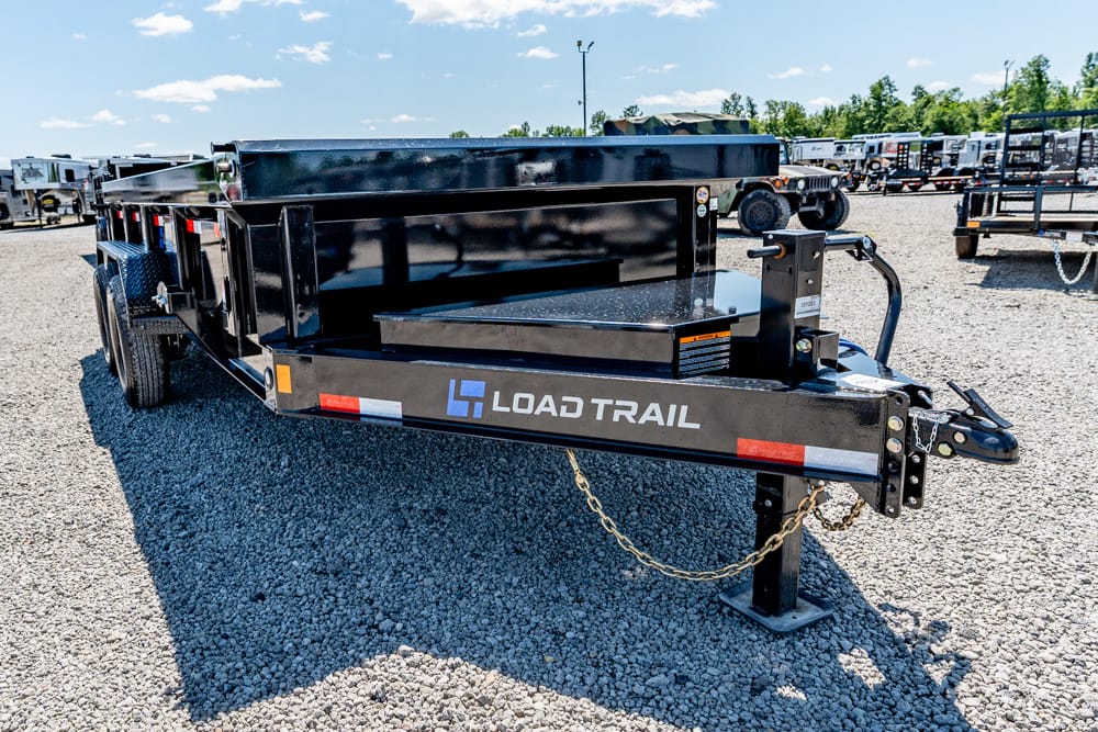 Load Trail black utility trailer with dual axles and hitch on a gravel lot, other trailers in the background, sunny day.