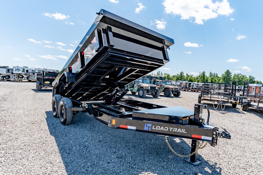 Black Load Trail dump trailer raised in a gravel lot, with other trailers in the background.