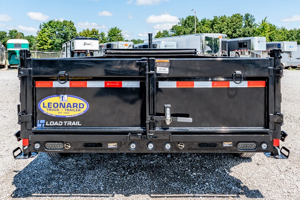 Rear view of a black Leonard Load Trail dump trailer in a lot, with other trailers in the background and a gravel ground surface.