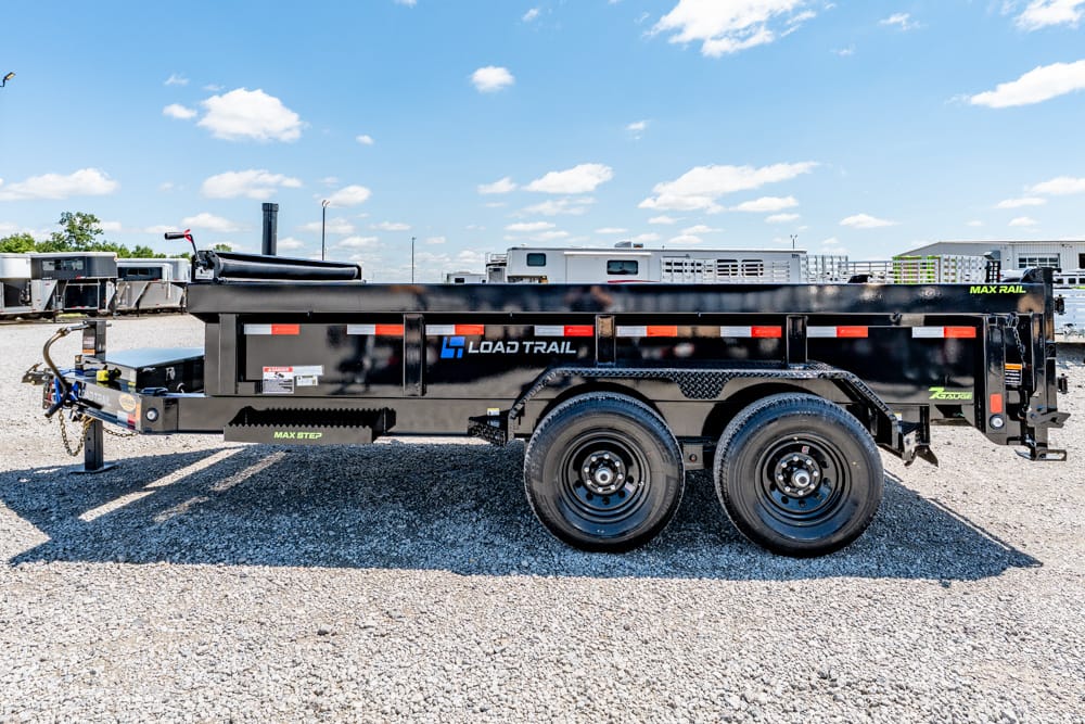 Side view of a black dual-axle Load Trail dump trailer on a gravel lot, showing the branding and safety reflectors