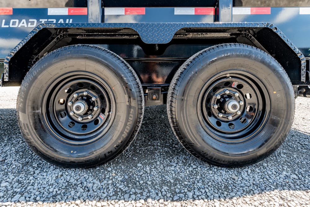 Dual truck wheels on a trailer with black metal frame, parked on gravel surface