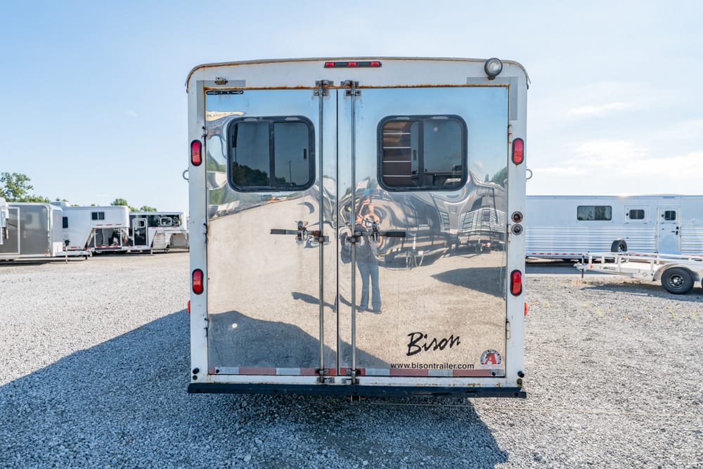 Shiny metal trailer back with two doors, windows, and 'Bison' logo, parked on gravel with other trailers nearby.