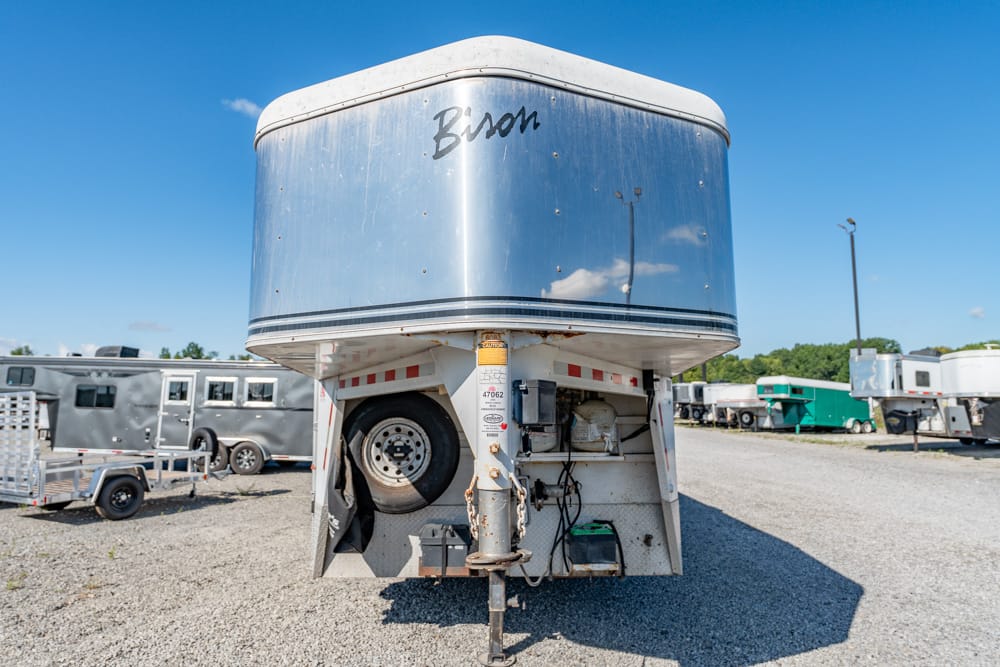 Front view of a shiny silver Bison horse trailer on a gravel lot, with other trailers in the background.
