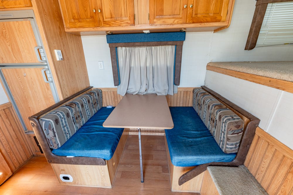 RV dinette with U-shaped booth seating, blue cushions, and a beige table