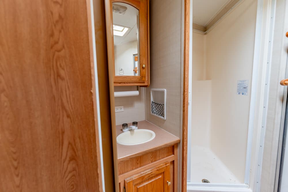 RV bathroom with wooden vanity, round sink, mirror cabinet, and a shower stall to the right.