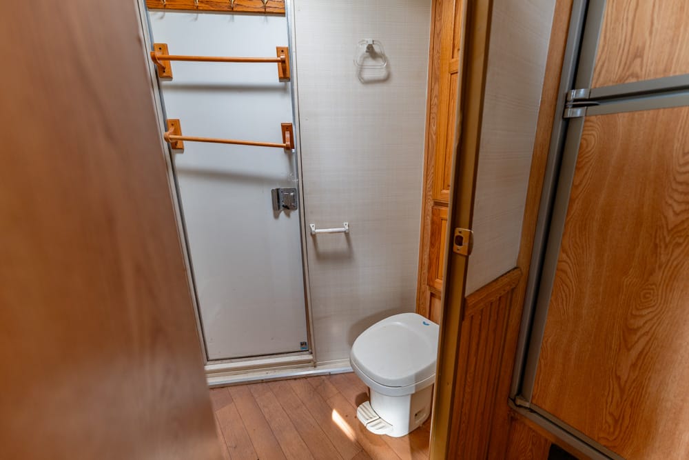 Small bathroom with a white toilet, shower door on the left, and wood-paneled walls and floor; orange towel bars mounted near the door.