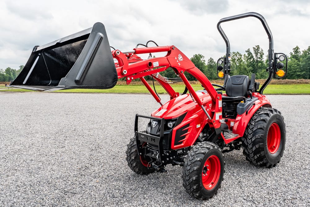 Red compact tractor with a front-end loader and large black bucket on a gravel lot