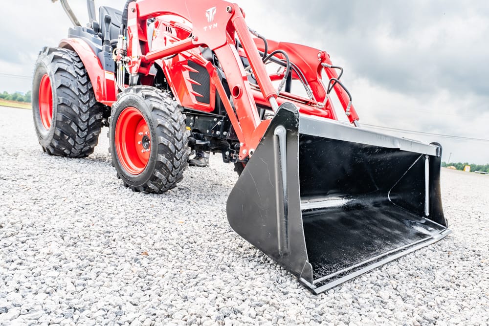 Red tractor with a large front-end loader on a gravel surface, viewed from the side.