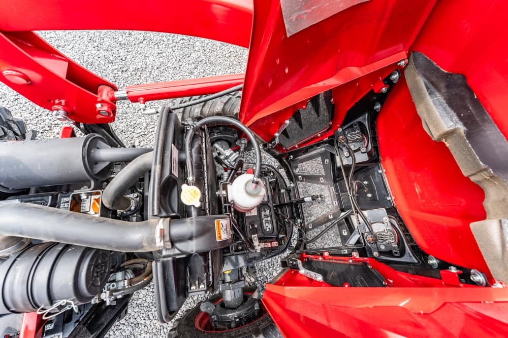 Close-up of a red vehicle's engine bay showing hoses, cables, and a battery amid red body panels.