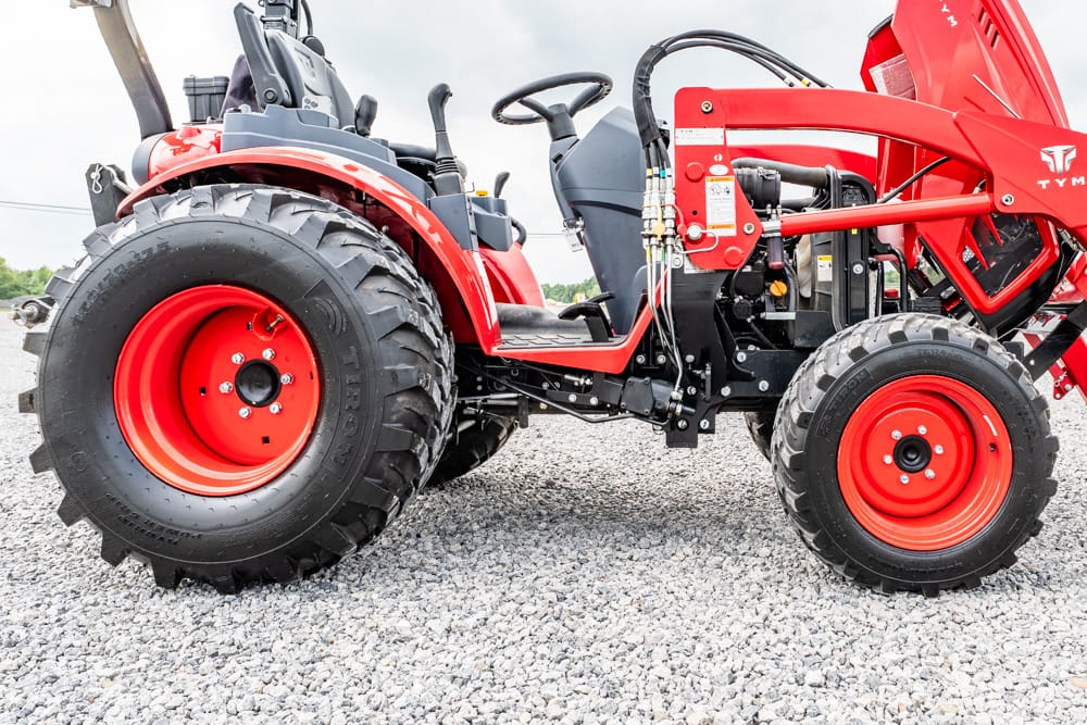 Red compact tractor on gravel, side view showing large rear wheel and red body panels with hydraulic components.