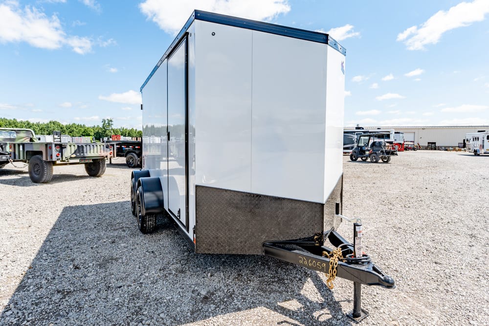 White enclosed cargo trailer with a diamond-plate front, parked on a gravel lot with other trailers in the background.