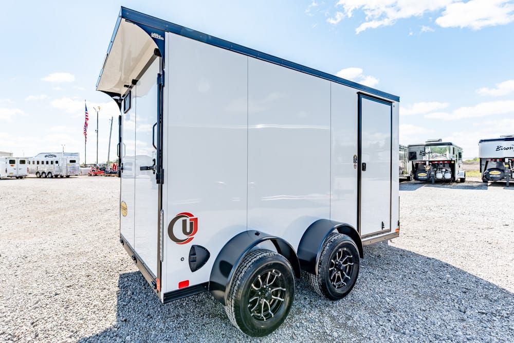 White enclosed cargo trailer with dual axles on a gravel lot, other trailers visible in the background.