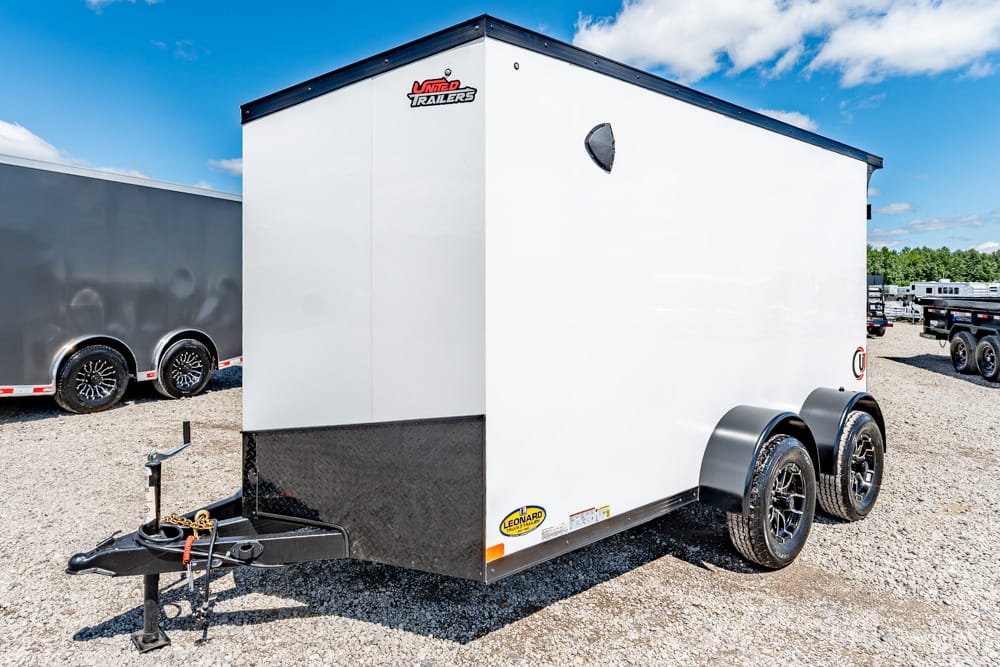 White enclosed cargo trailer with dual axles and black wheel wells parked on a gravel lot.