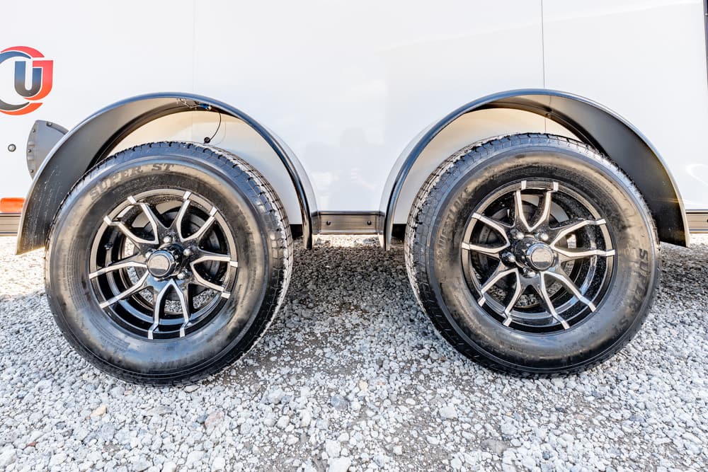 Dual black alloy wheels on a white trailer above a gravel surface, shown side-by-side.